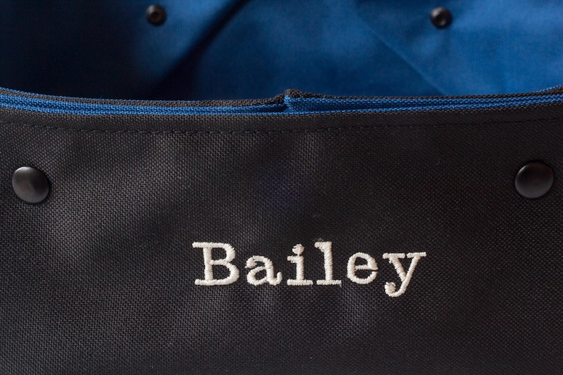 K&ouml;nnte beinhalten: Schwarze Canvas-Tragetasche mit blauer Innenausstattung und dem Namen "Bailey" in wei&szlig; gestickt.