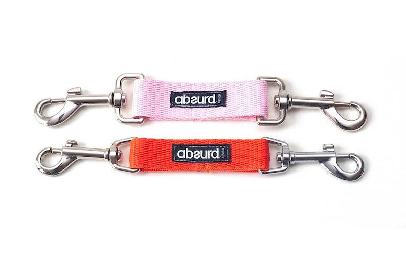 May include: Two dog leash attachments with silver clips. The top attachment is pink with the word "absurd" printed on it. The bottom attachment is orange with the word "absurd" printed on it.