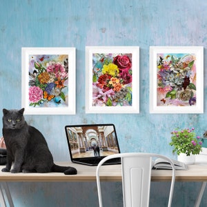 Puede incluir: Tres impresiones florales enmarcadas con una variedad de flores coloridas y mariposas. Las impresiones est&aacute;n colgadas en una pared azul claro. Un gato gris est&aacute; sentado en una mesa de madera frente a las impresiones. Un ordenador port&aacute;til y una silla blanca tambi&eacute;n est&aacute;n en la mesa.