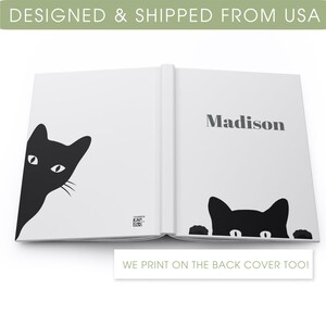 May include: A white hardback journal with a black cat peeking out from the left side of the cover. The right side of the cover has the name "Madison" printed in black. The back cover also features a black cat peeking out.