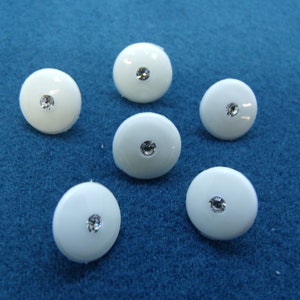 May include: Six white round buttons with a clear rhinestone in the center.