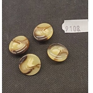 Könnte beinhalten: Vier braune und weiße Knöpfe mit einem Wirbelmuster. Die Knöpfe sind oval geformt und haben eine glänzende Oberfläche.