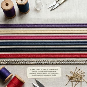 Puede incluir: Ocho tiras de ribete de piel sintética de 10 mm en morado, beige, rosa, azul marino, negro, rojo y estampado de serpiente. Incluye carretes de hilo de madera, un dedal, tijeras de metal y una etiqueta que dice RUBAN / BIAIS PASSEPOIL SIMILI CUIR.