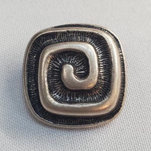 Op de afbeelding: Zilverkleurige, vierkante broche met een verhoogd spiraalontwerp. De broche heeft een getextureerde rand en een wervelend patroon in het midden. Het sieraad is geplaatst tegen een witte achtergrond.