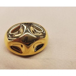 Puede incluir: Un anillo de color dorado, abstracto, tridimensional, de forma ovalada con una superficie lisa y brillante.