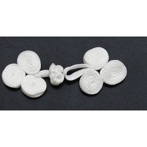 Peut inclure: Fermeture en nœud chinois en tissu blanc avec une boucle au centre. Le nœud est composé de plusieurs boucles circulaires.