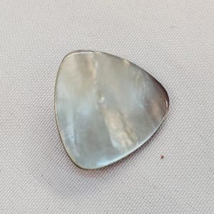 May include: A pearlescent, teardrop-shaped guitar plectrum with a silver edge. The plectrum has a smooth, iridescent surface with a subtle gradient of colours. The plectrum is a musical instrument accessory.