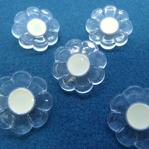 Peut inclure: Cinq boutons en plastique transparent en forme de fleur avec des centres blancs.