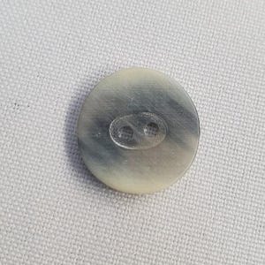 Peut inclure: Un bouton ovale à deux trous. Le bouton présente un aspect marbré avec des nuances de gris et de crème. Le bouton est fait d'un matériau lisse, possiblement naturel.