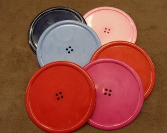 Può includere: Sei sottobicchieri rotondi con un design a bottone. I sottobicchieri sono di vari colori, tra cui blu, rosa, rosso e nero.