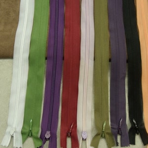 May include: Assortment of 10 zipper tapes in various colors, including white, green, purple, red, pink, beige, olive green, dark purple, black, and peach. The zipper tapes are all the same length and have a metal slider.