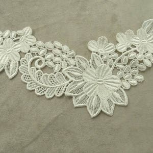 Pode incluir: Renda branca com um design floral. A renda apresenta flores e folhas delicadas.