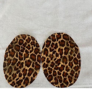 Puede incluir: Dos círculos de tela con estampado de leopardo marrón y beige sobre un fondo blanco.