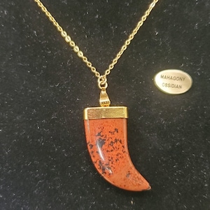 Peut inclure: Un collier en chaîne dorée avec un pendentif en obsidienne acajou en forme de dent. Le pendentif est serti d'un métal doré. L'étiquette indique "Obsidienne acajou".