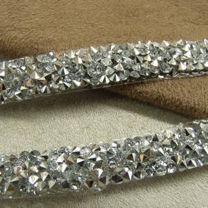 Puede incluir: Dos filas de ribete de strass plateado con respaldo transparente. El ribete está hecho de pequeños strass puntiagudos.