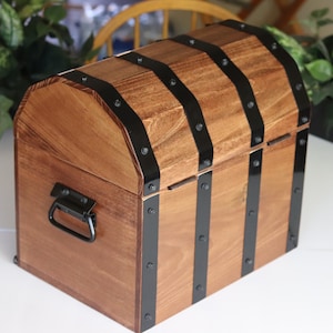 May include: A wooden treasure chest with a hinged lid and a black metal handle. The chest is decorated with black metal bands and rivets.