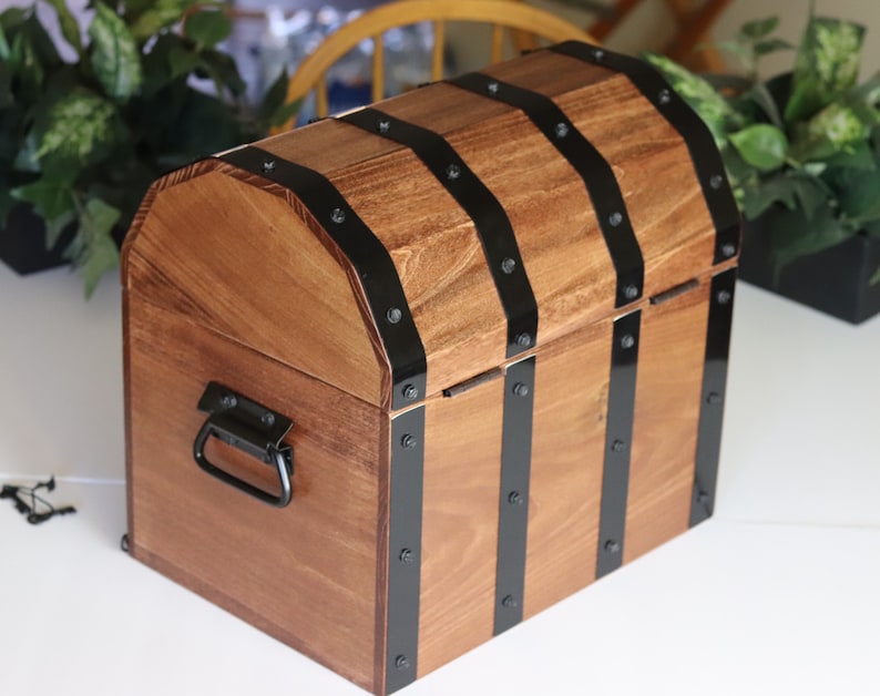 May include: A wooden treasure chest with a hinged lid and a black metal handle. The chest is decorated with black metal bands and rivets.