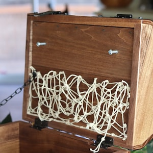 May include: A wooden treasure chest with a hinged lid, a metal chain, and a white rope net lining the inside.