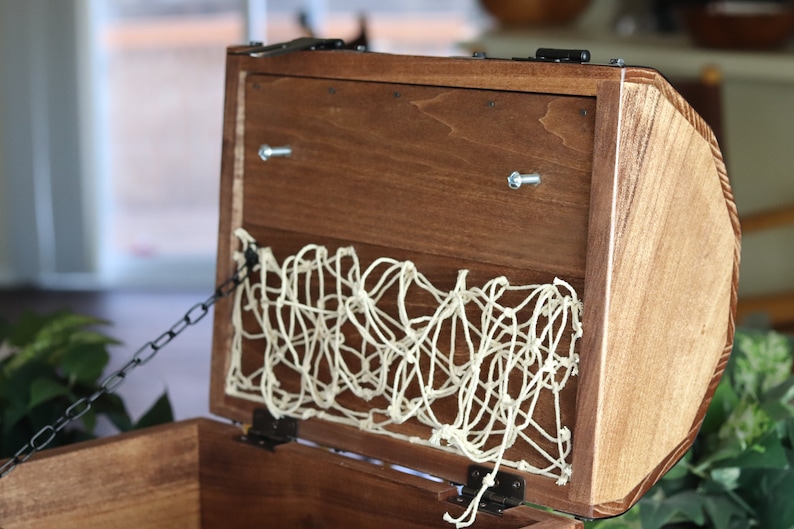 May include: A wooden treasure chest with a hinged lid, a metal chain, and a white rope net lining the inside.