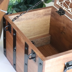 May include: A wooden box with a hinged lid and a metal chain. The box has black metal accents and a net lining inside the lid.