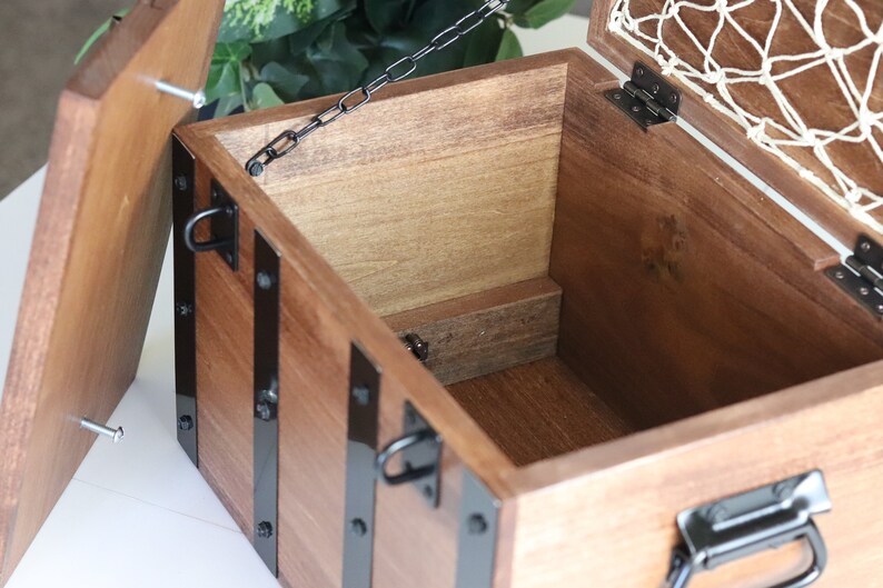 May include: A wooden box with a hinged lid and a metal chain. The box has black metal accents and a net lining inside the lid.