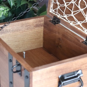 May include: A wooden treasure chest with a hinged lid and a metal chain. The chest has black metal accents and a white net lining the inside of the lid.