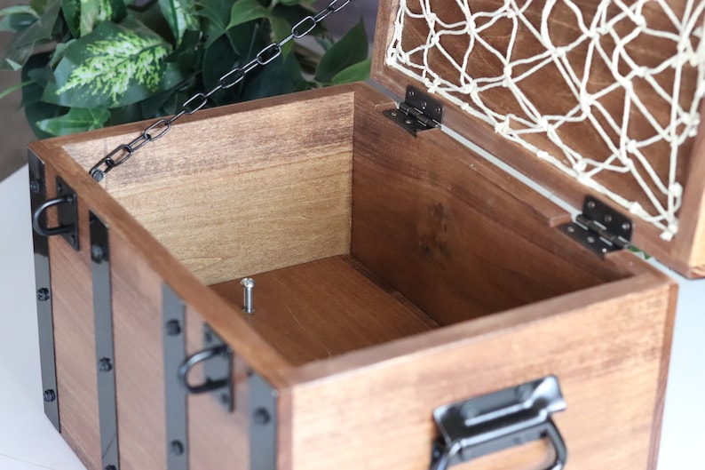 May include: A wooden treasure chest with a hinged lid and a metal chain. The chest has black metal accents and a white net lining the inside of the lid.