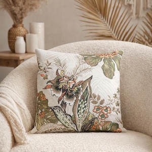 May include: A square throw cushion featuring a detailed botanical print with large flowers and foliage in shades of olive green, burnt orange, and cream. The fabric has a textured appearance with a repeating pattern of leaves and floral blooms.