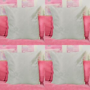 May include: Four white throw pillows with a subtle embossed pattern, arranged on a pink sofa.