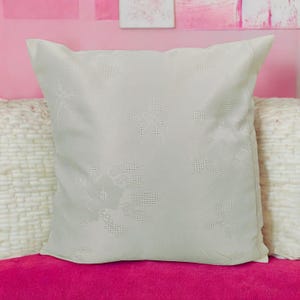 May include: A white throw pillow with a subtle floral pattern. The pillow is made of a soft, textured fabric and has a square shape.