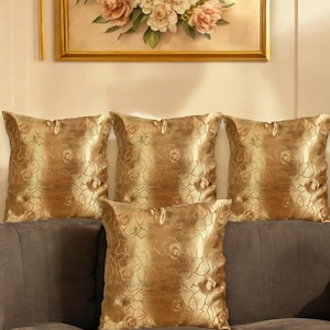 May include: Four gold throw pillows with a floral pattern. The pillows are arranged on a brown couch.