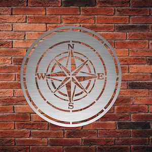 May include: A silver metal compass with a brushed finish and a circular design. The compass features the cardinal directions N, S, E, and W.