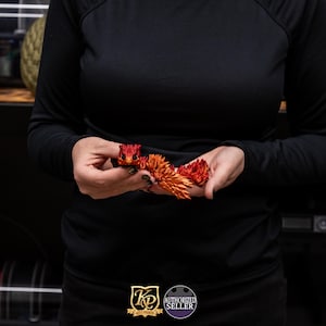 May include: A hand holding a red and orange dragon figurine. The dragon is made of a textured material and has a detailed design.