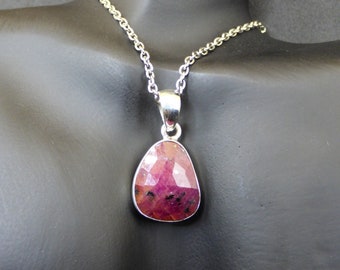 May include: A silver chain necklace with a pink gemstone pendant. The pendant is faceted and has a teardrop shape.