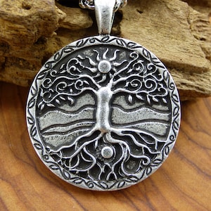 May include: Silver pendant necklace featuring a detailed tree of life design with a sun and moon at the top and bottom. The pendant is round and has a silver chain.
