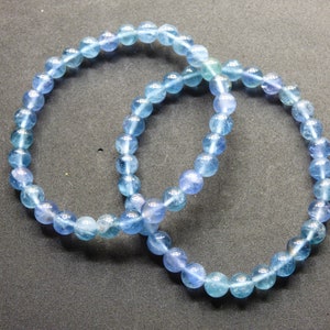 May include: Two blue gemstone bracelets made of round beads. The bracelets are intertwined and are on a gray background.
