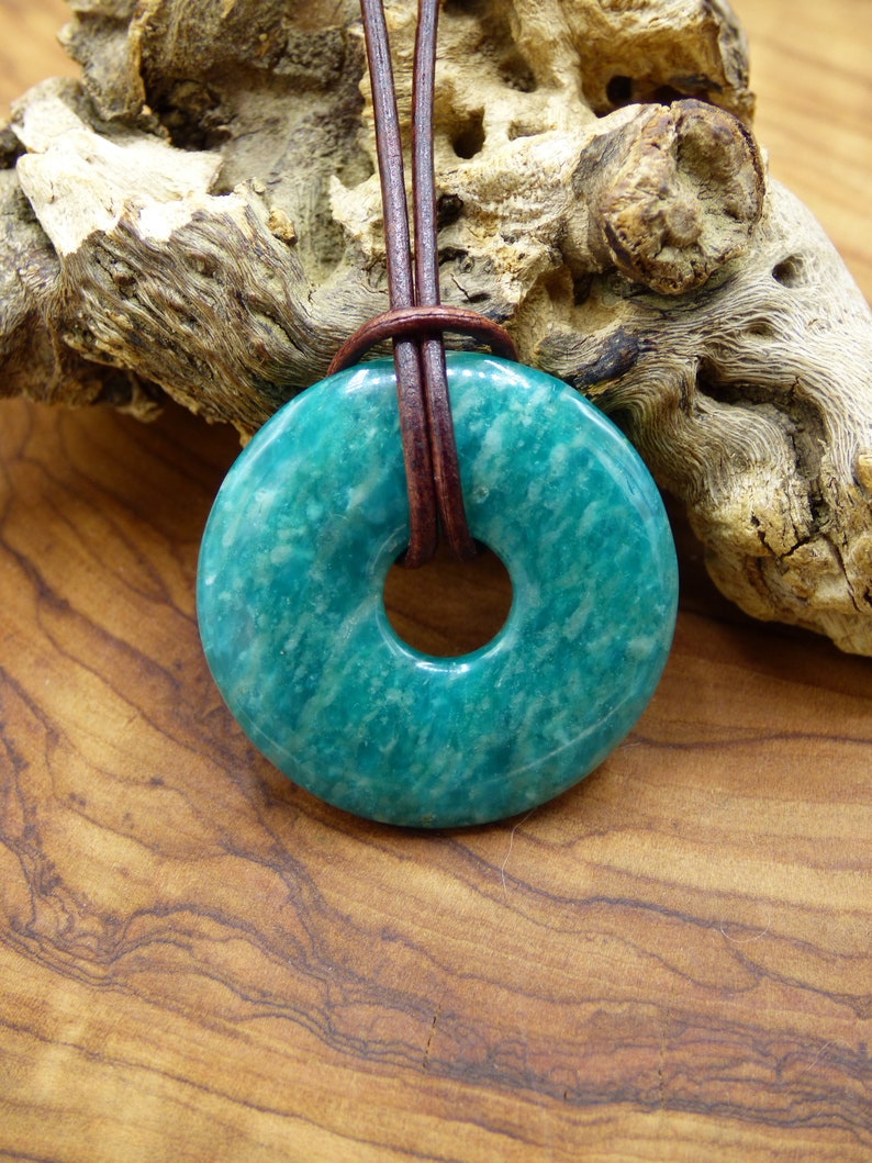 Pode incluir: Um pingente de pedra aventurina verde-azulada em forma de rosquinha, com um cord&atilde;o de couro marrom.