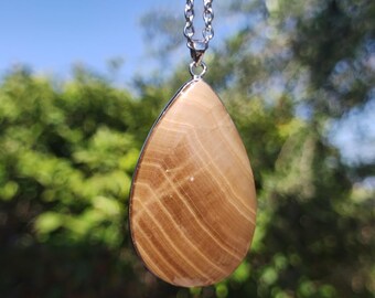 May include: A teardrop-shaped pendant necklace with a light brown and white striped stone. The pendant is hanging from a silver chain.