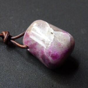May include: A pink and white gemstone pendant on a brown leather cord. The gemstone has a rough, natural texture.