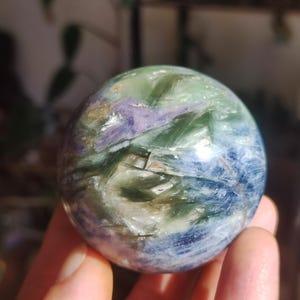 Könnte beinhalten: Eine polierte Kugel aus blauem, grünem und violettem Kristall. Der Kristall hat ein wirbelndes Muster aus Farben und eine glatte, glänzende Oberfläche.