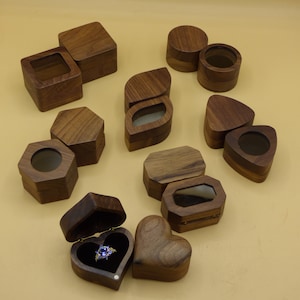 Può includere: Assortimento di scatole per anelli in legno di varie forme, tra cui quadrata, rotonda, a forma di cuore e esagonale. Alcune scatole hanno un coperchio in vetro trasparente, mentre altre hanno un coperchio in legno massiccio. Le scatole sono in legno scuro e hanno una finitura naturale.