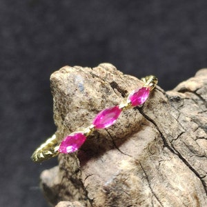 Puede incluir: Un anillo de oro con tres piedras preciosas rosas en forma de marquesa engastadas en una banda delicada.