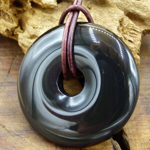 K&ouml;nnte beinhalten: Schwarzer Obsidian-Anh&auml;nger mit Spiraldesign, an einem braunen Lederband.