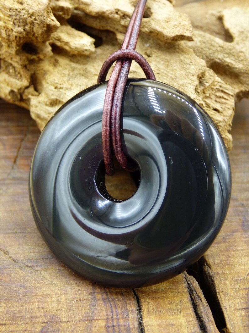 K&ouml;nnte beinhalten: Schwarzer Obsidian-Anh&auml;nger mit Spiraldesign, an einem braunen Lederband.
