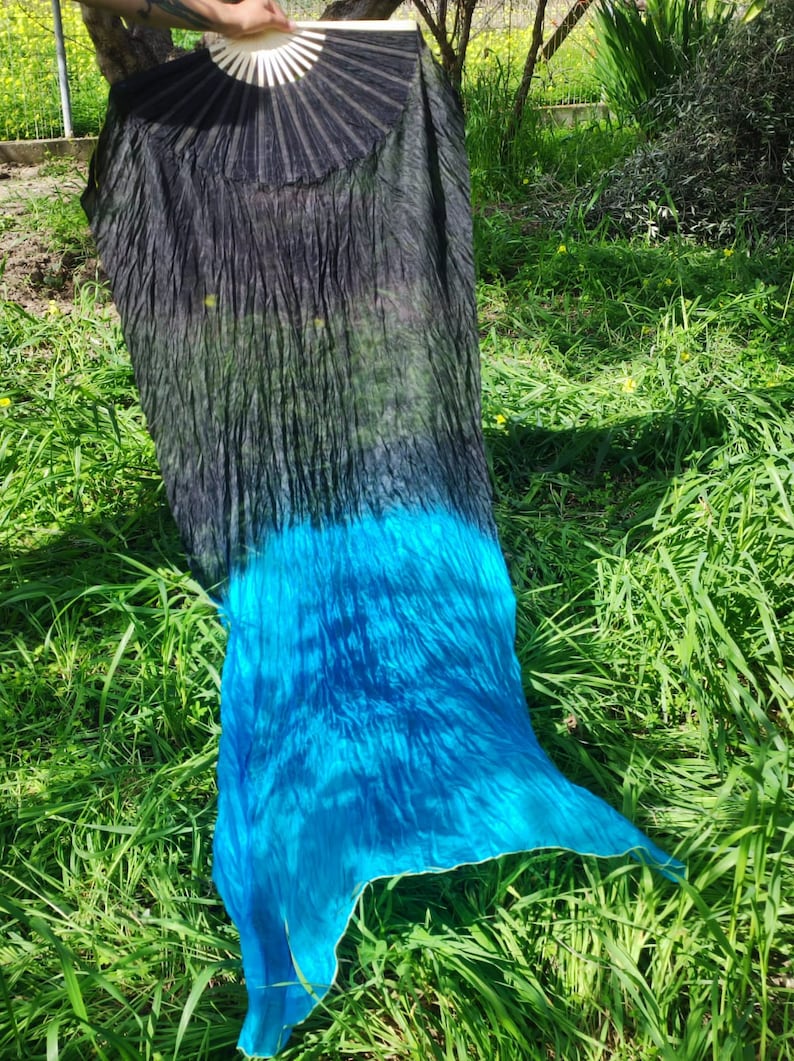 May include: A black and blue silk dance veil with a gradient color effect. The veil is flowing in the wind and is partially covering a green grassy area.