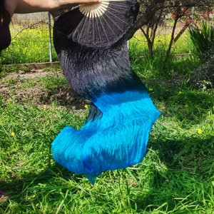 May include: A black and blue silk dance veil with a black fan. The veil is flowing in the wind and the fan is open.