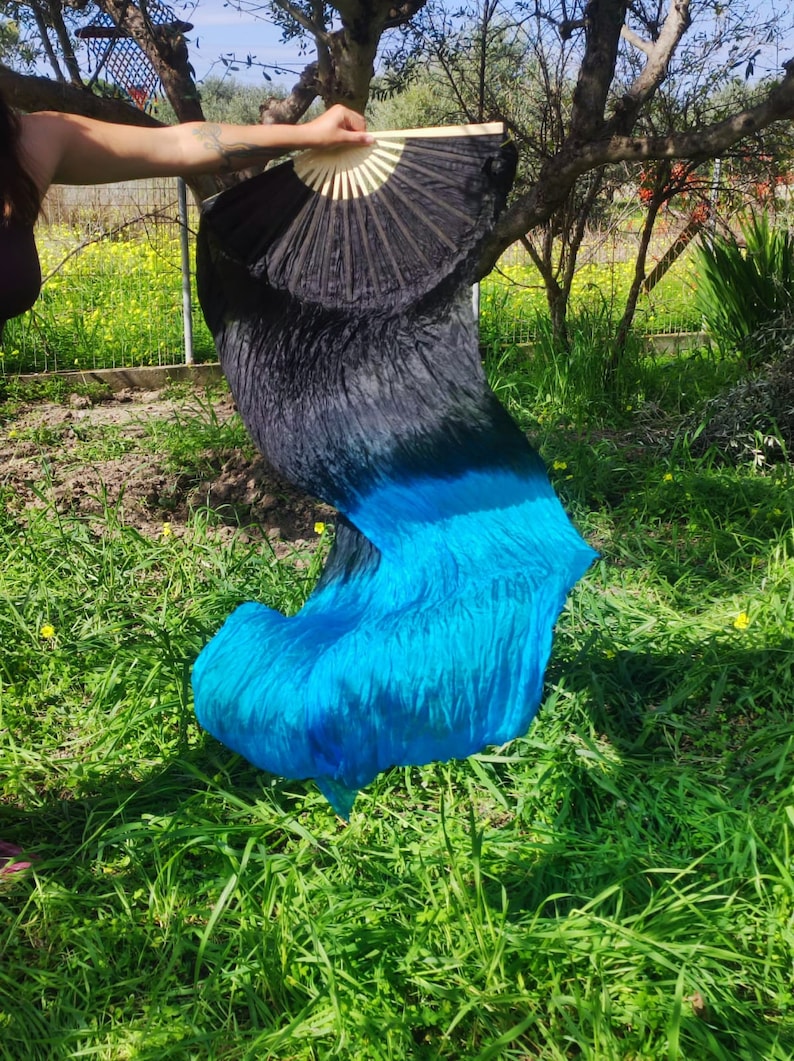 May include: A black and blue silk dance veil with a black fan. The veil is flowing in the wind and the fan is open.