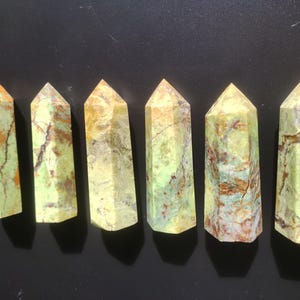 May include: Six polished gemstone obelisks with a faceted design. The stones have a mix of colors, including green, orange, and brown. Each obelisk is approximately 4 inches tall.