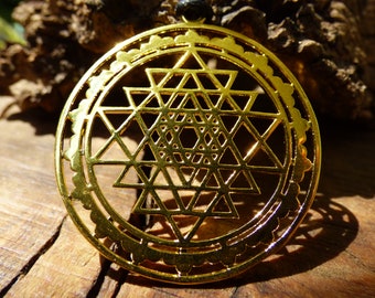 May include: A gold-colored pendant featuring a Sri Yantra, a sacred geometric symbol in Hinduism, with intricate details and a circular border.