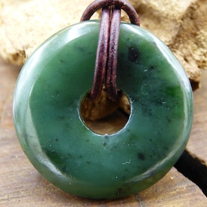 Pu&ograve; includere: Un ciondolo in giada verde a forma di anello, con un cordino in pelle marrone.